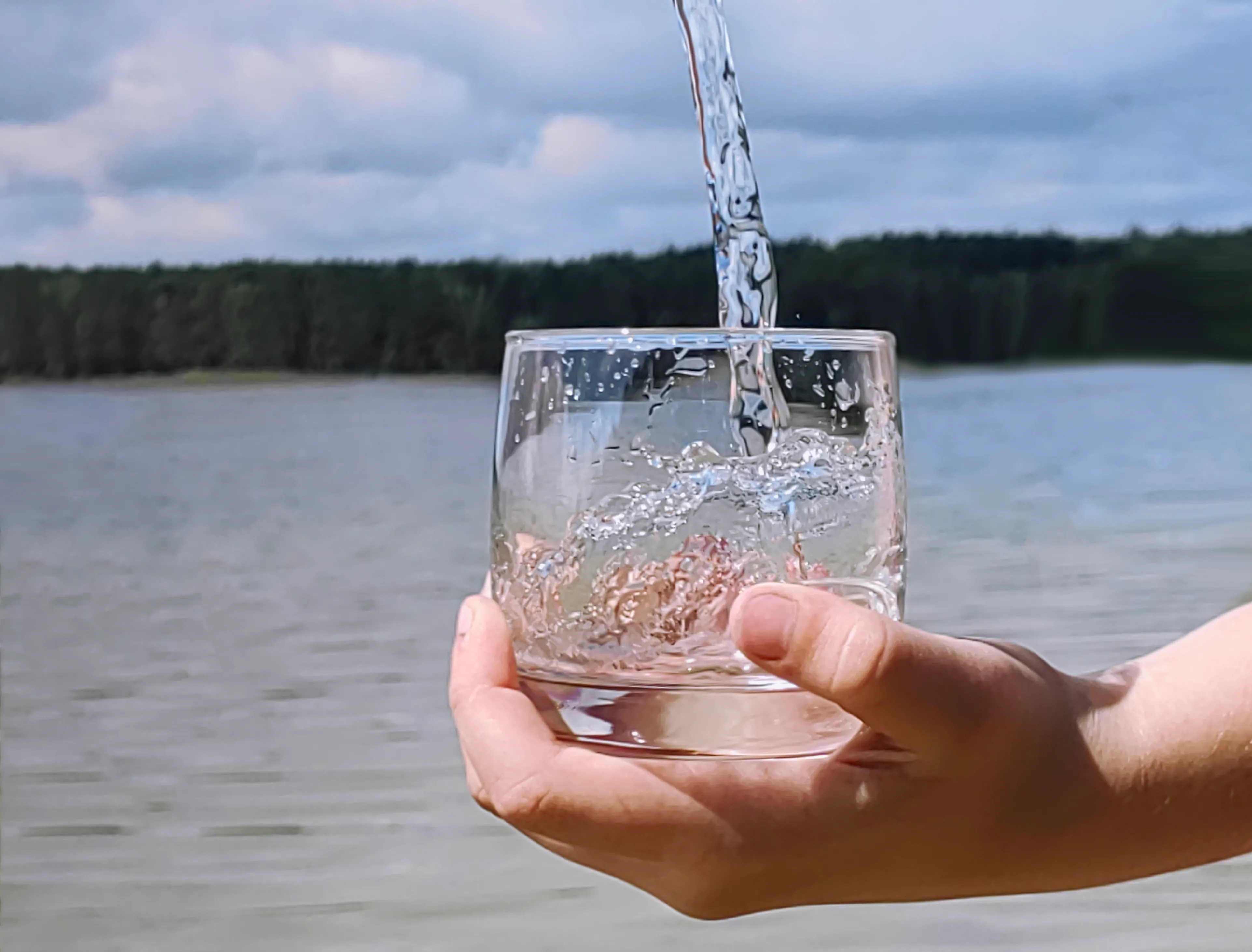 gloved hand holding test tube by river
